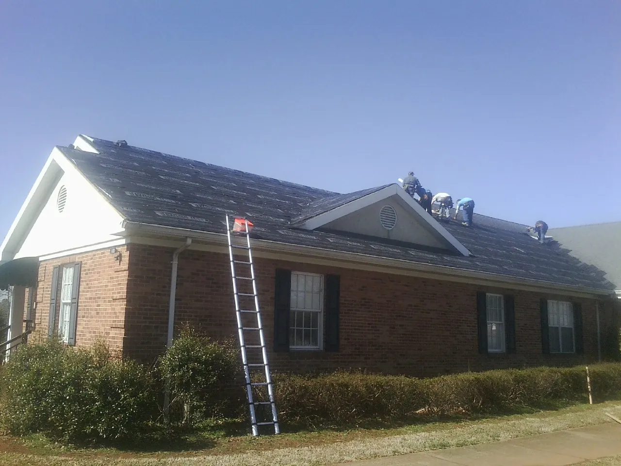 Crew tearing shingles off a brick ranch roof with a ladder set — Metal Roof Repair work by our crew in Darby