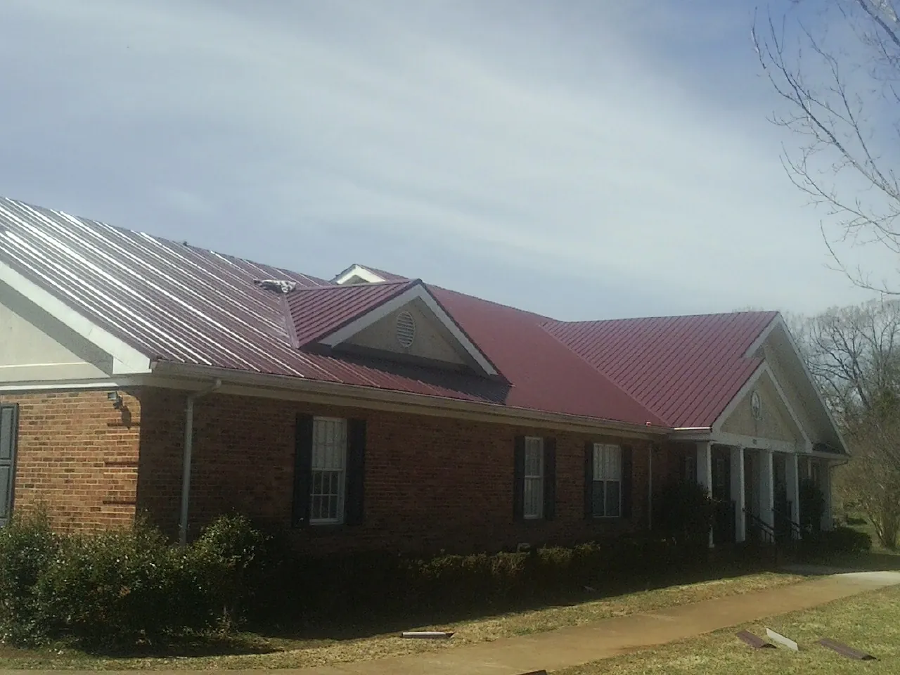 Red metal roof with gabled entries on a long brick building, from a Hail Damage Roof Repair job in Darby