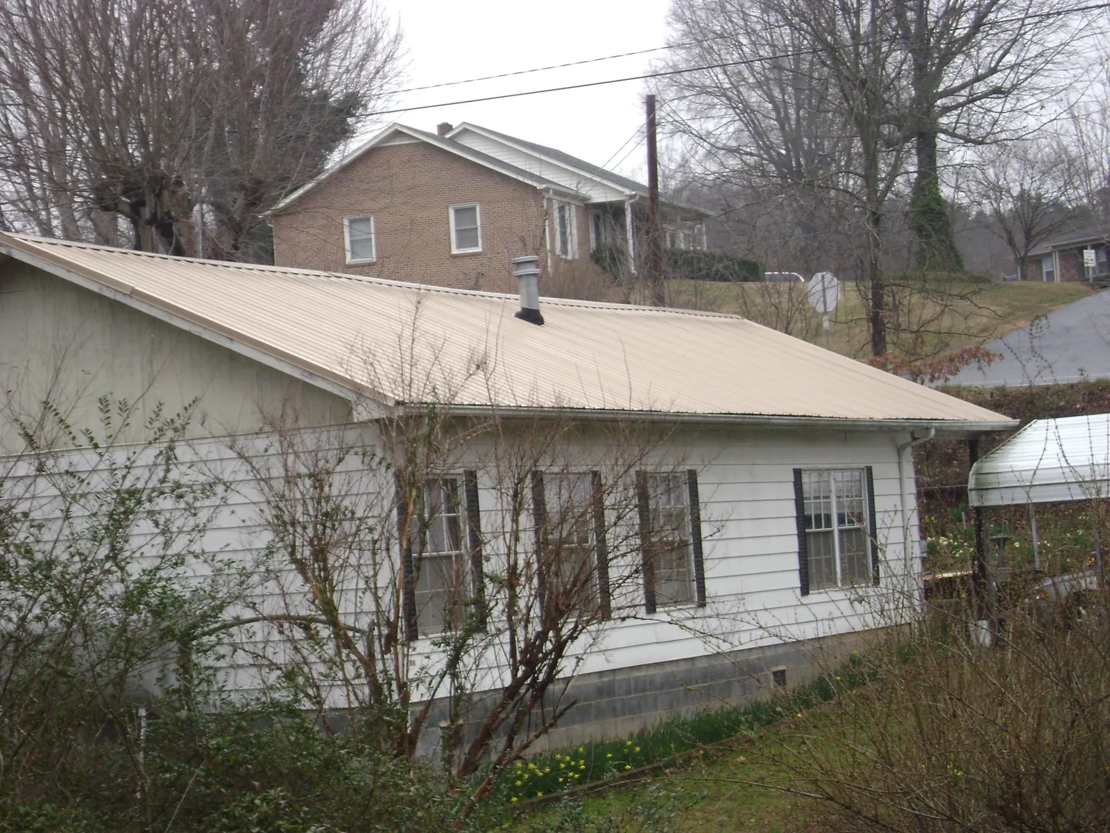 Tan metal roof on a white sided house set into a hillside — Commercial Roofing by Roofing Brothers in Darby